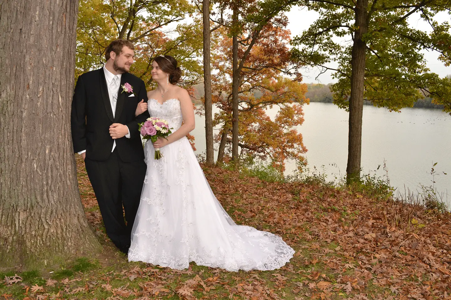 Bride and groom together beside a lake beneath autumn trees