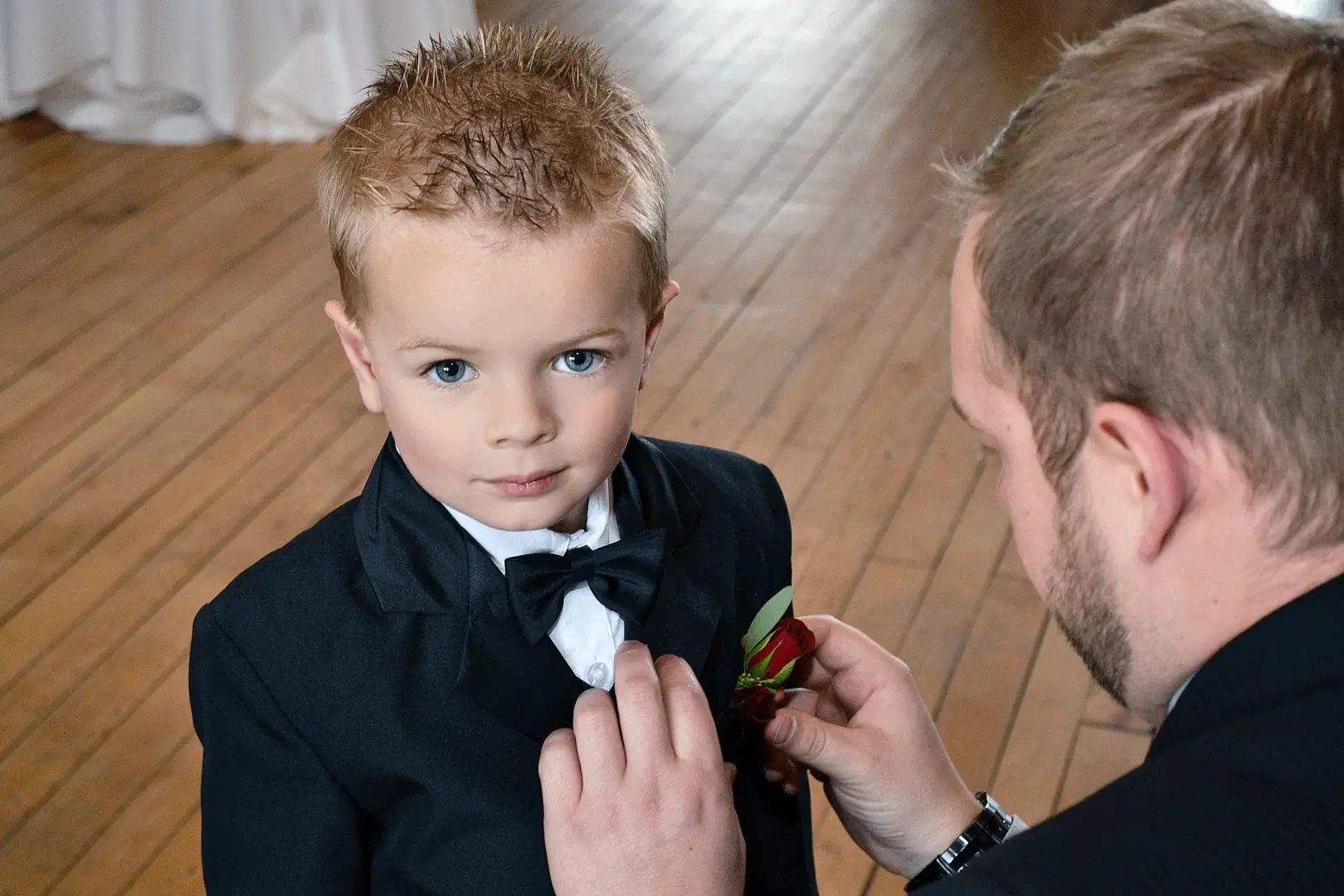 Young boy in a suit having his boutonniere adjusted before a wedding